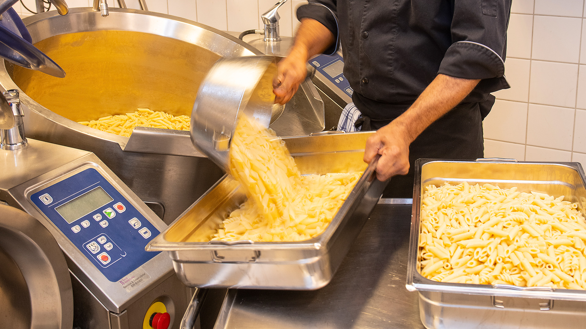 Kock i storkök häller upp pasta.