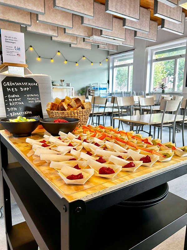 Ett bord med små serveringsskålar fyllda med grönsaksstavar och rödbetsdipp, placerat i en ljus matsal