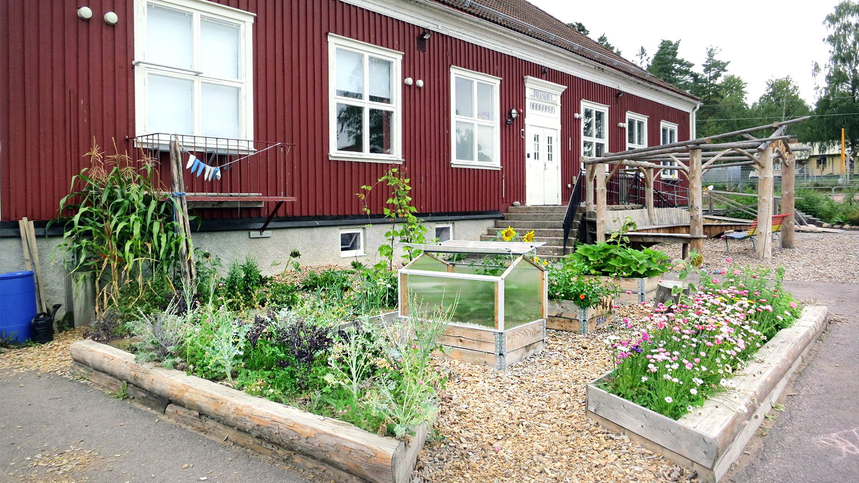 Skolbyggnad med odlingar framför.