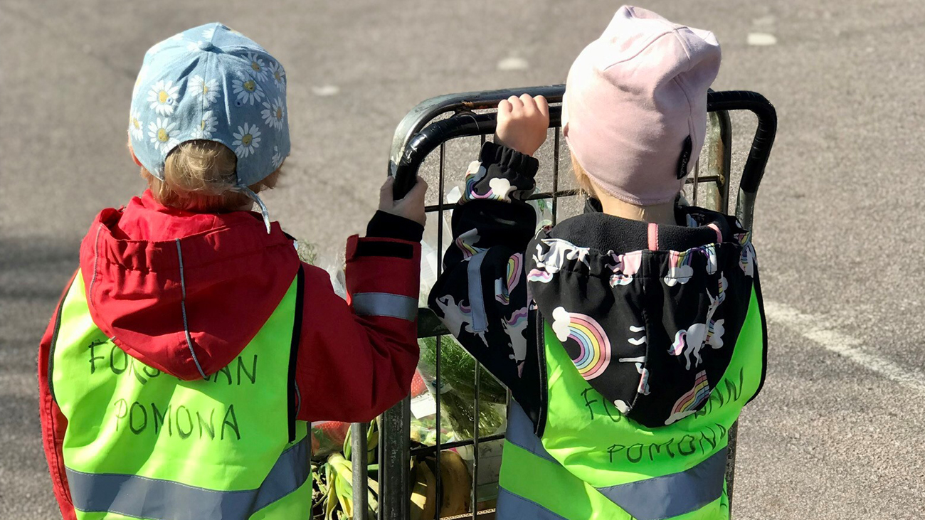 Förskolebarn som kör överblivna grönsaker och frukter i en vagn.