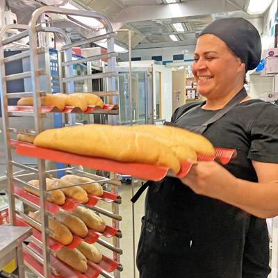 En kvinna i ett storkök håller fram en plåt med bröd.