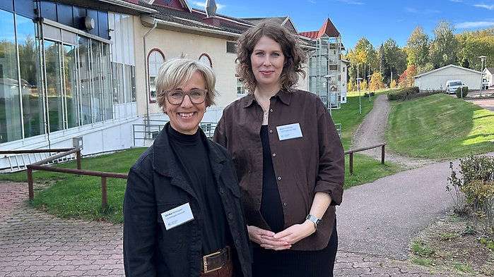 Två kvinnor ler mot kameran utanför byggnad.
