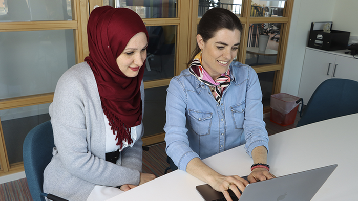 Afraa Hajjar och Linda Törner sitter tillsammans framför en bärbar dator.