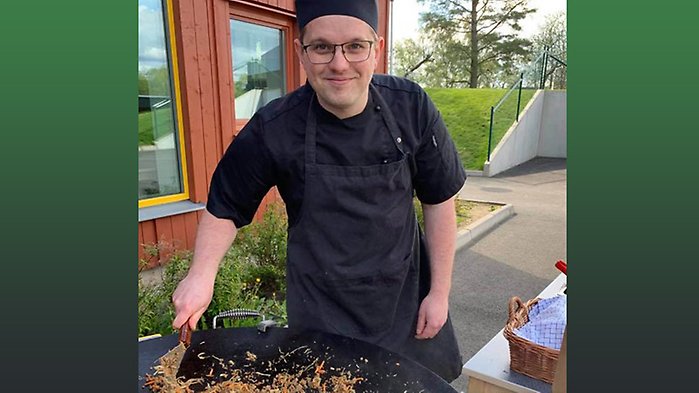 En manlig kock står och lagar mat vid en stekhäll utomhus.