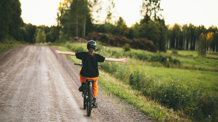 Ung tjej cyklar på en grusväg och har släppt händerna från styret.