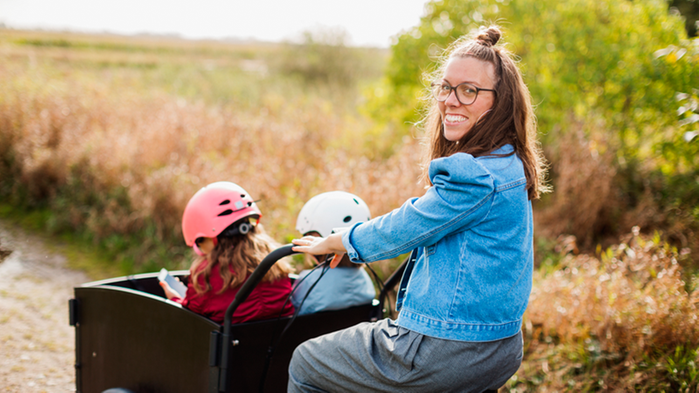 En kvinna kör två barn på en lådcykel.